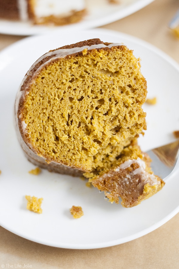 A close up image of a slice of pumpkin cake with a bite on a fork in front of it on the white plate.
