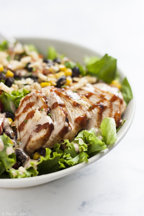 A close up image of sliced grilled chicken in the bowl of BBQ chicken salad drizzled with BBQ sauce and BBQ ranch dressing.