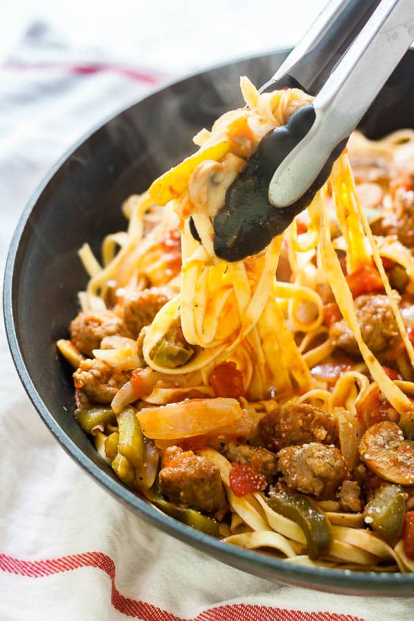 A pan of Sausage and peppers pasta with some tongs lifting some of the pasta up.
