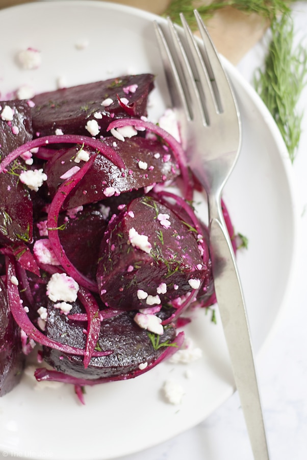 An overhead image of half of a white plate of beet salad with a fork on the side of it.