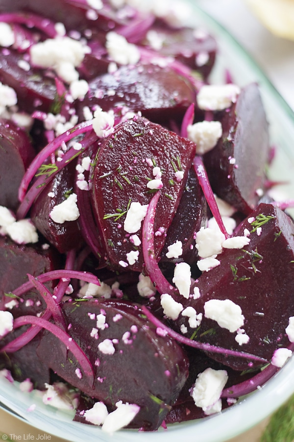 A large serving dish of roasted beets i na salad with onions and feta cheese.