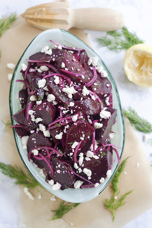 An overhead image of the large teal bowl of this beet salad recipe on a cutting board surrounded by fresh dill, a half a squeeze lemon and a lemon reamer.