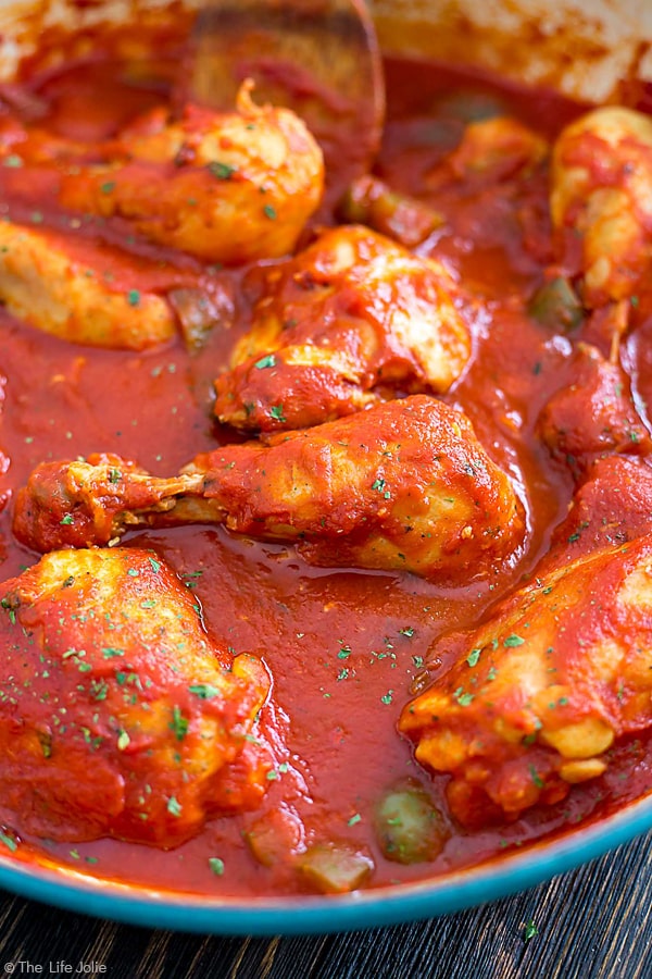 A close up image looking into a pan full of chicken cacciatore and zooming in on a drum stick.