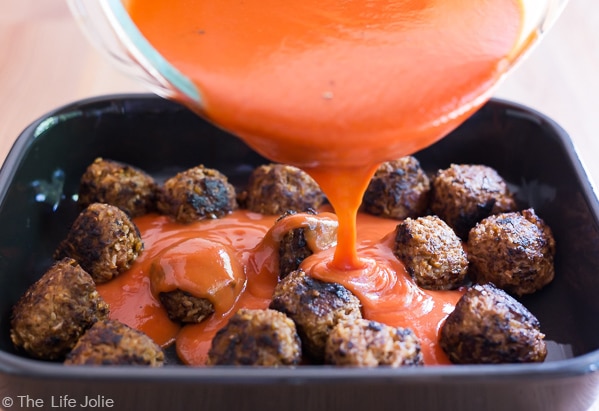 The Classic Porcupine Meatballs sauce being poured over the browned meatballs in a baking pan.