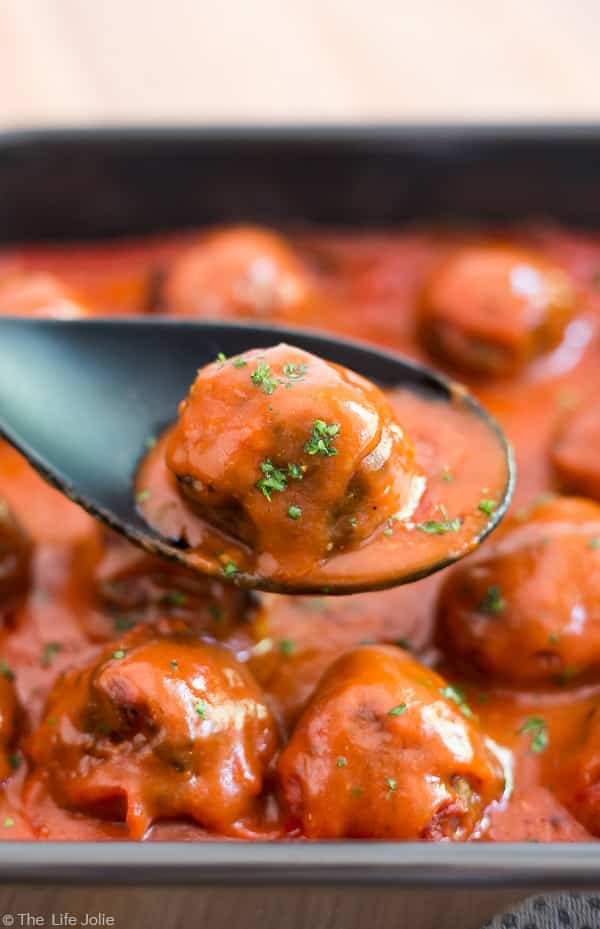 A Classic Porcupine Meatball being picked up with a black spoon from a dark pan full of other meatballs.