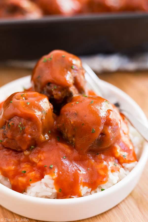 A close up image of Classic Porcupine Meatballs on a white plate with a dark pan of meatballs behind it out of focus.