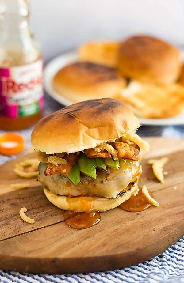 A photo of Sweet Chili Turkey Burgers on a wooden cutting board with bun tops and a bottle of Frank's RedHot Sweet Chili sauce in the background out of focus.