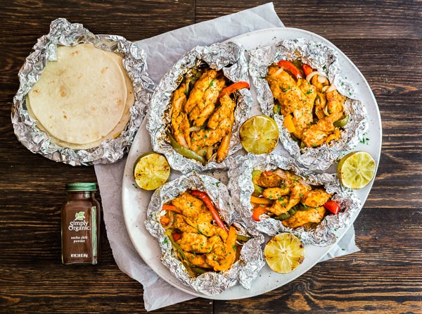 An overhead image of Foil Packet Chicken Fajitas on a platter with some tortillas and Simply Organic Ancho Chili Powder.