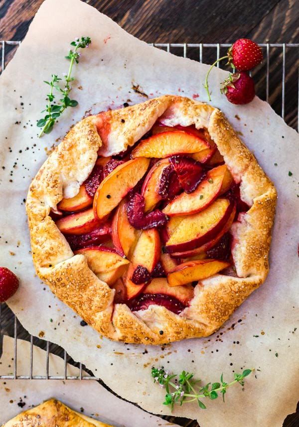 An overhead shot of the Nectarine and Strawberry Galette with Thyme on parchment paper woth some sprigs of fresh thyme and strawberries around it.