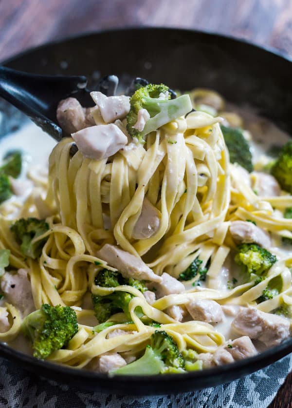 A spoon pulling Creamy Chicken and Broccoli Pasta out of the pan.