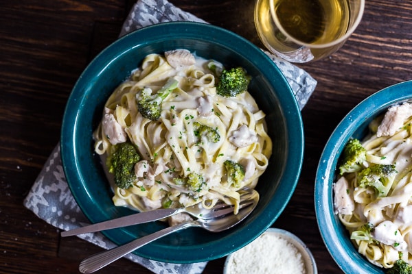 An overhead image of Creamy Chicken and Broccoli Pasta in a blue bowl with another bowl on the side and a glass of wine.