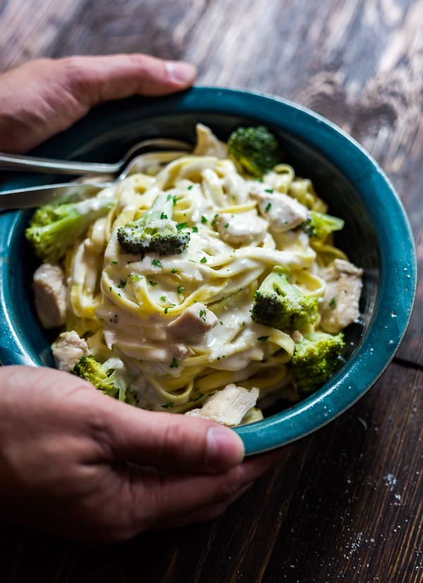 An image of hands holding a blue bowl of Creamy Chicken and Broccoli Pasta.