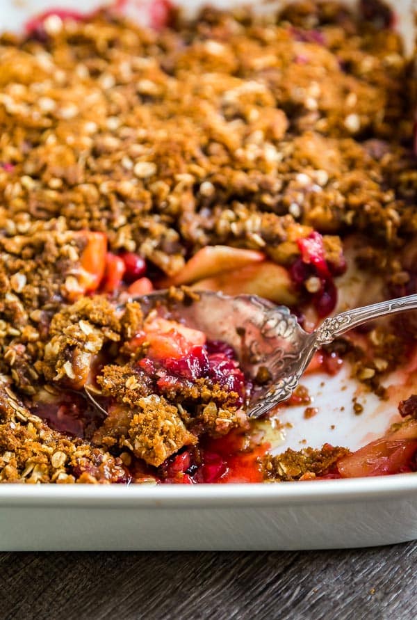 A pan of Cranberry Apple Crisp Recipe with Oatmeal Ginger Snap Topping with some of it missin and the serving spoon in the pan.