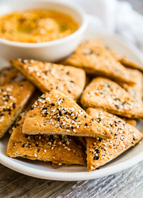 A plate of Everything Pita Chips with a bowl of hummus in the background.