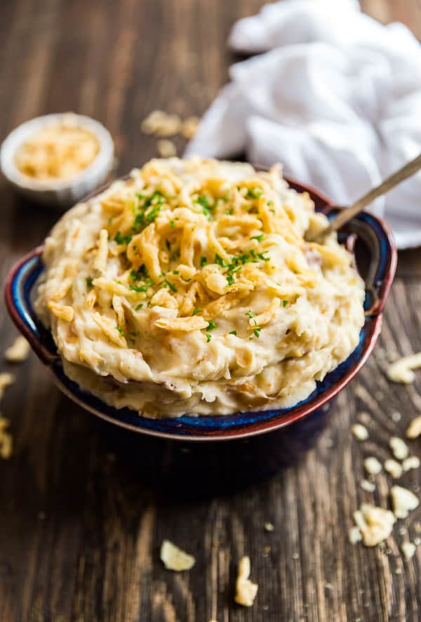 French Onion Creamy Mashed Potatoes in a bowl with french fried onions on top and some scattered around it.