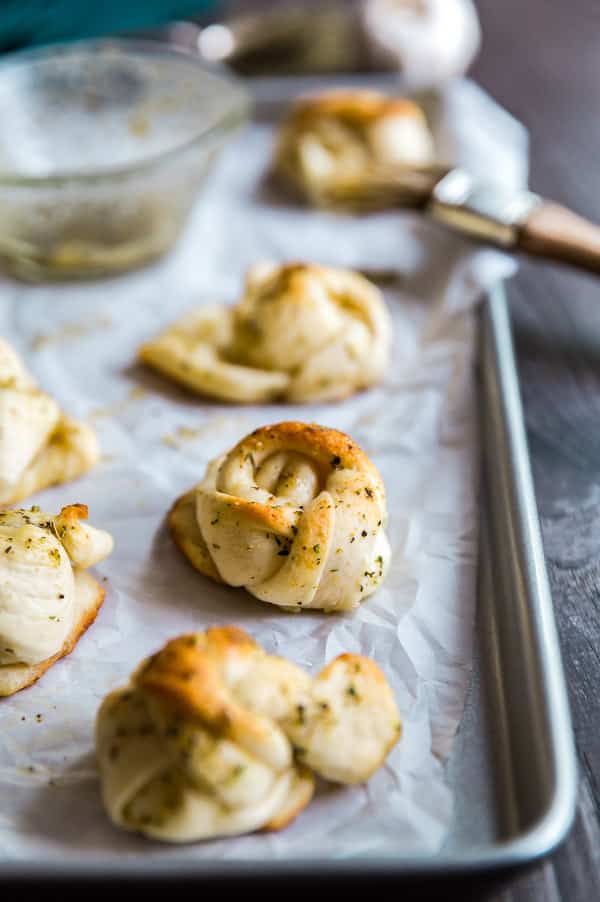 A close of of a Cheesy Garlic Knot on a pan with others surrounding it.